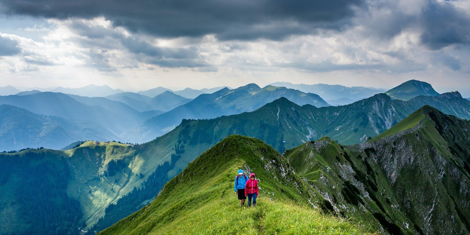 Walkers following a green ridge through blue mountain scenery
